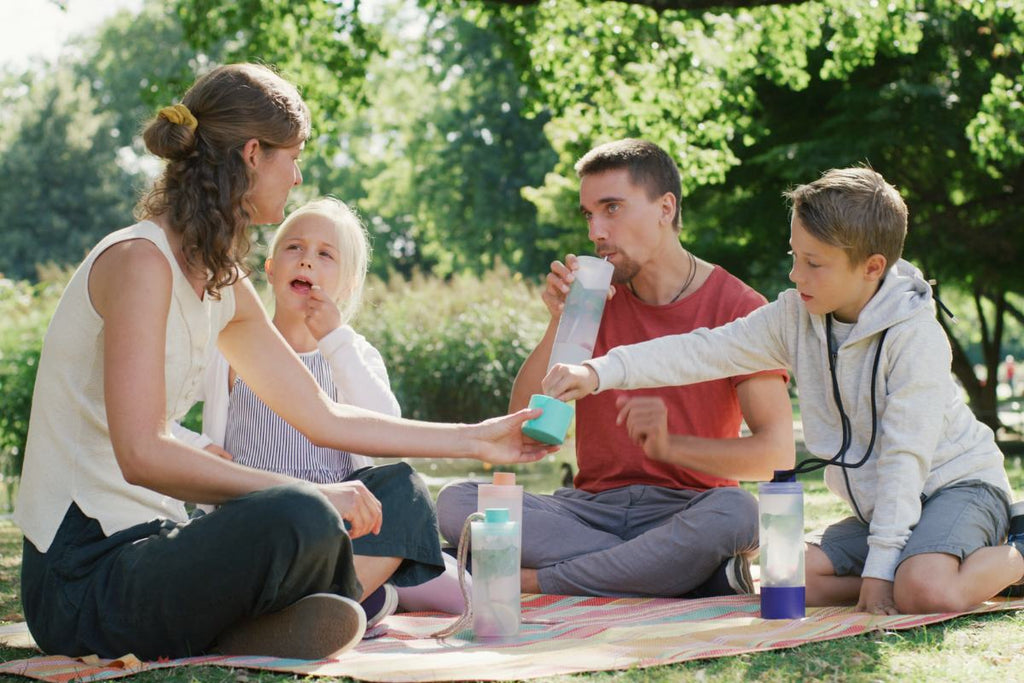 Familie beim Picknick Ausflug. Ein Kind greift in die Snackbox, der Vater trinkt aus dem Becher