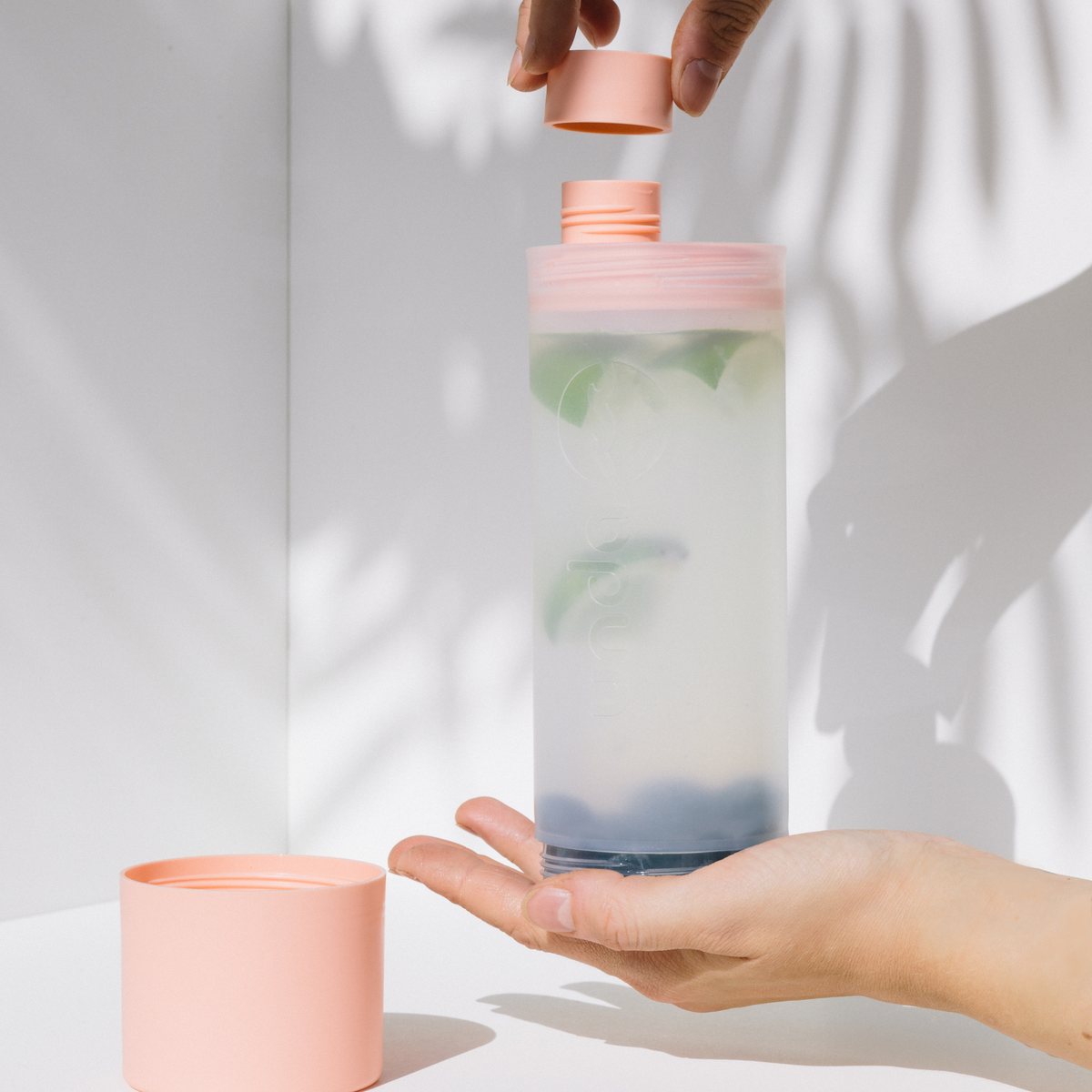 Eine Hand öffnet die UNDA mit Infused Water, daneben steht der abgeschraubte Becher