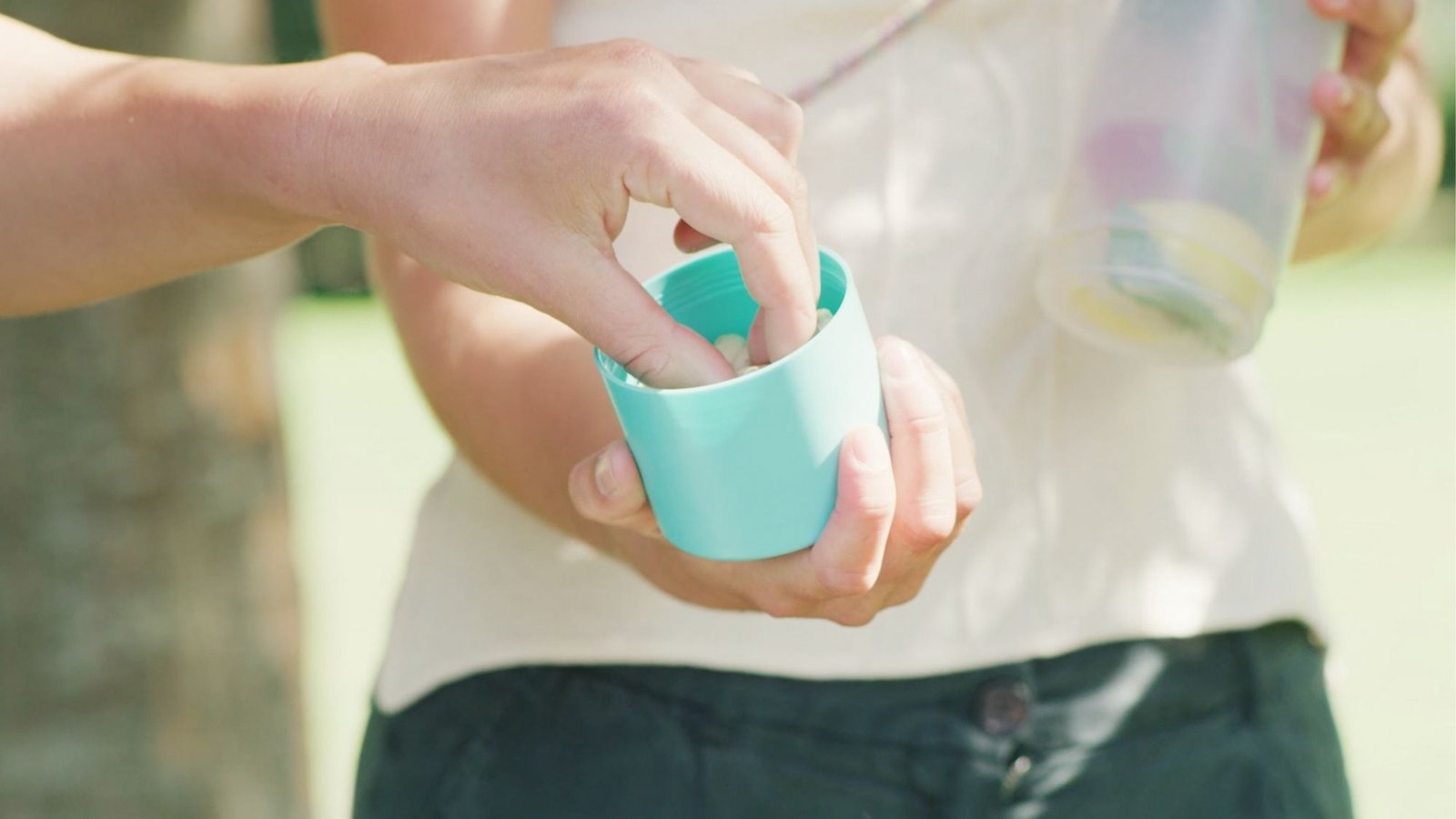 Hand hält den türkisen UNDA Becher, in der anderen Hand die gefüllte Flasche