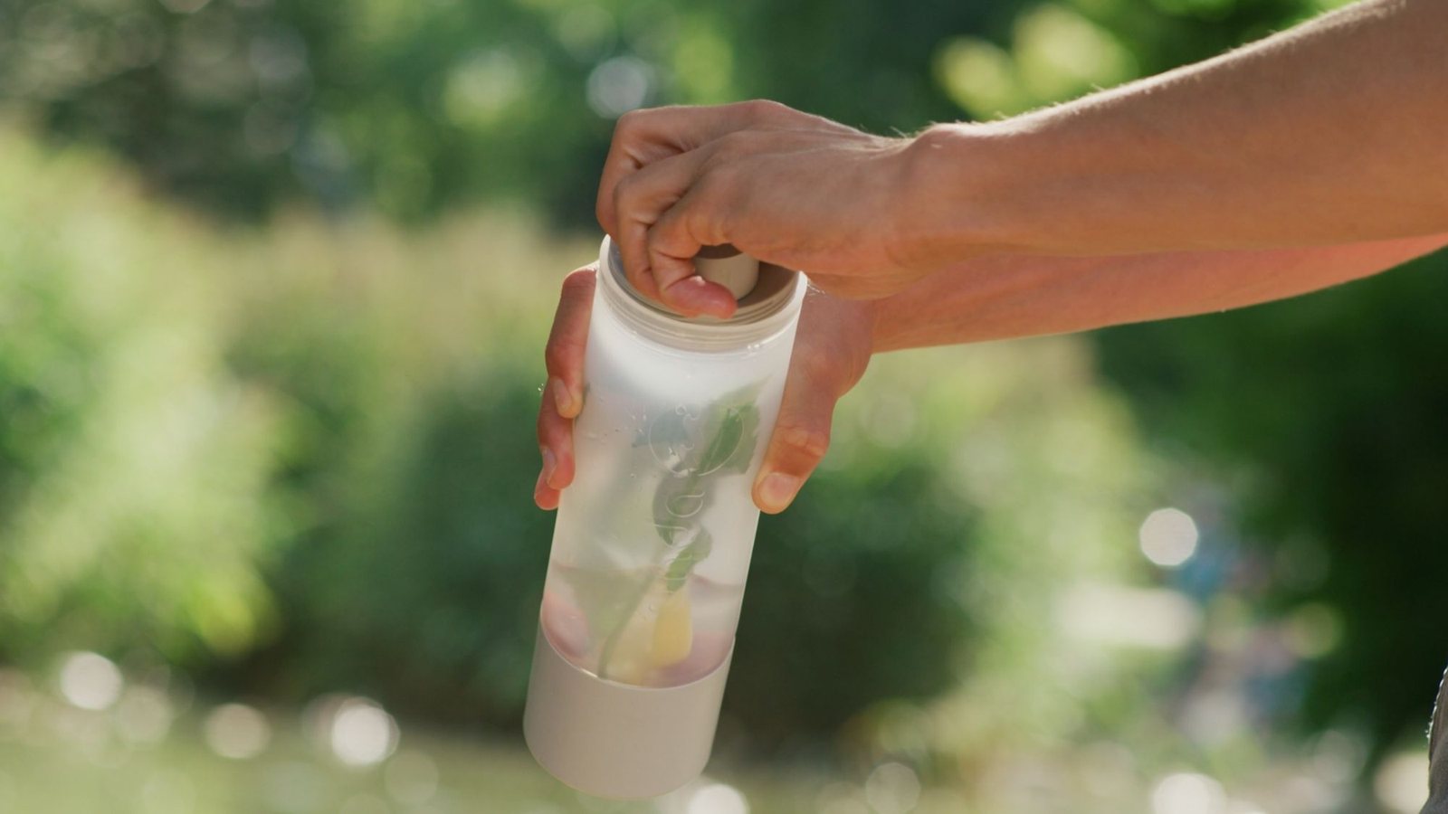 Hand hält die UNDA mit Wasser, Minze und Zitrone im Freien